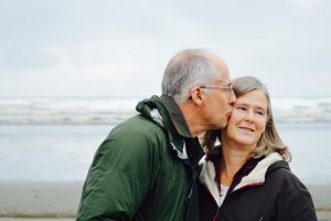 retired couple man kissing wife on cheek at a beach